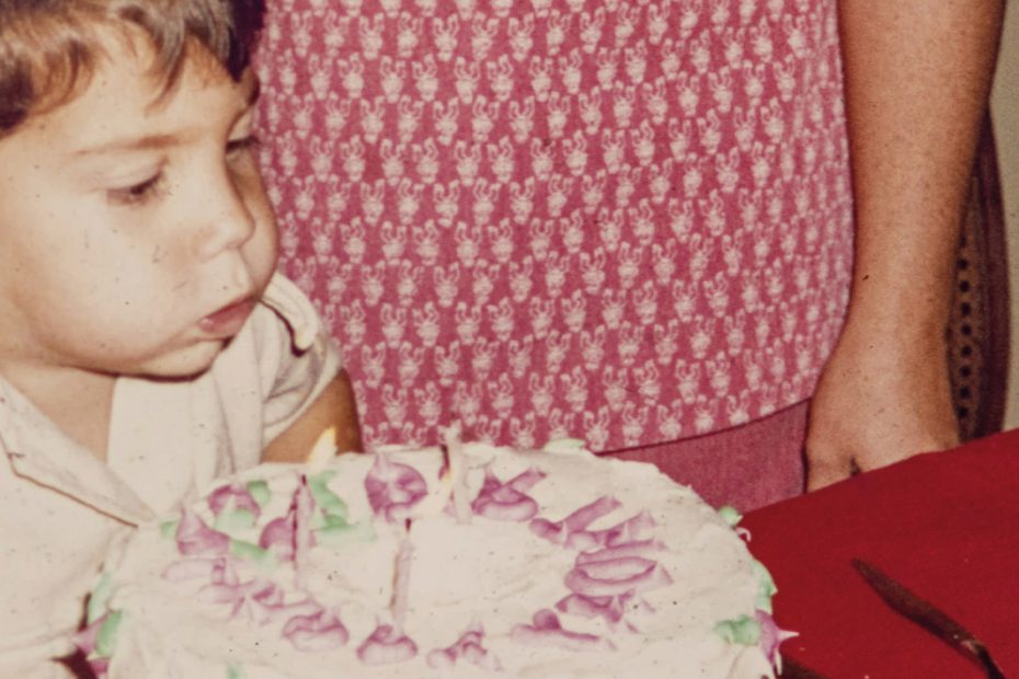 Un bambino soffia sulle candeline di una torta di compleanno. La foto non è attuale, risale ai primi anni Ottanta. Dietro di lui si intravede la madre.